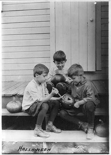 Three boys on porch steps cutting faces in pumpkins.